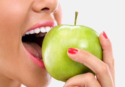 Imagem ilustrando uma mulher mastigando uma maçã sem se preocupar com os dentes, pois os implantes podem ajudar em uma melhoria na mastigação